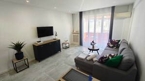 Ein modernes Wohnzimmer mit Flachbildfernseher, einer Couch, einem Couchtisch und einem Blumentopf.