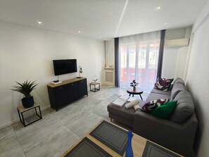 A modern living room with a flat-screen TV, a sofa, a coffee table, and a potted plant. - Appart 2 chambres – calme & lumineux – proche tram (Nice)