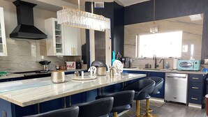 A modern kitchen with a marble countertop, black bar stools, a built-in oven, and a microwave. - New on VRBO! New Construction, Stylish Mega RV Garage House (Lake Havasu City)
