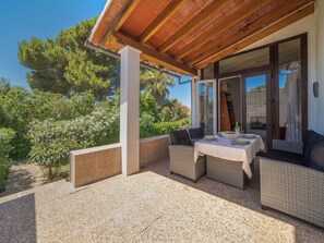 Un espace extérieur aménagé, abrité et doté de mobilier en osier, avec une table dressée pour le repas, et offrant une vue sur la verdure et les arbres.