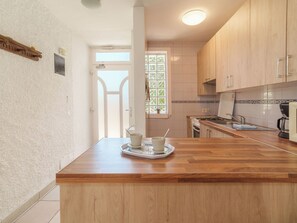 A kitchen with wooden cabinets, a countertop, a window with a view, and a door leading to another room. - Vacation home Calma by Interhome (Porto Cristo)
