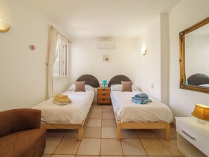 A hotel room with two single beds, a small table, a chair, a mirror, and a lamp. - Vacation home Calma by Interhome (Porto Cristo)