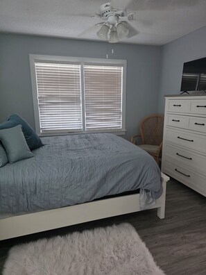Ein Schlafzimmer mit Bett, Kommode, Stuhl und Deckenventilator.