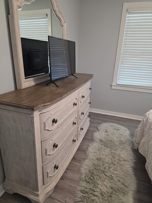 A bedroom with a dresser, a mirror, a fluffy rug, and a window with blinds. - Enjoyable 3-bedroom house with AC in Murrells Inlet (Murrells Inlet)