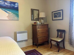 A room with a bed, a wooden dresser, a chair, a radiator, and a painting on the wall. - Pentz Howe House Apartment, (Charlottetown)