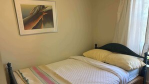 A single bed with a wooden frame, a striped blanket, and two pillows. A framed picture hangs on the wall above the bed. - Pentz Howe House Apartment, (Charlottetown)