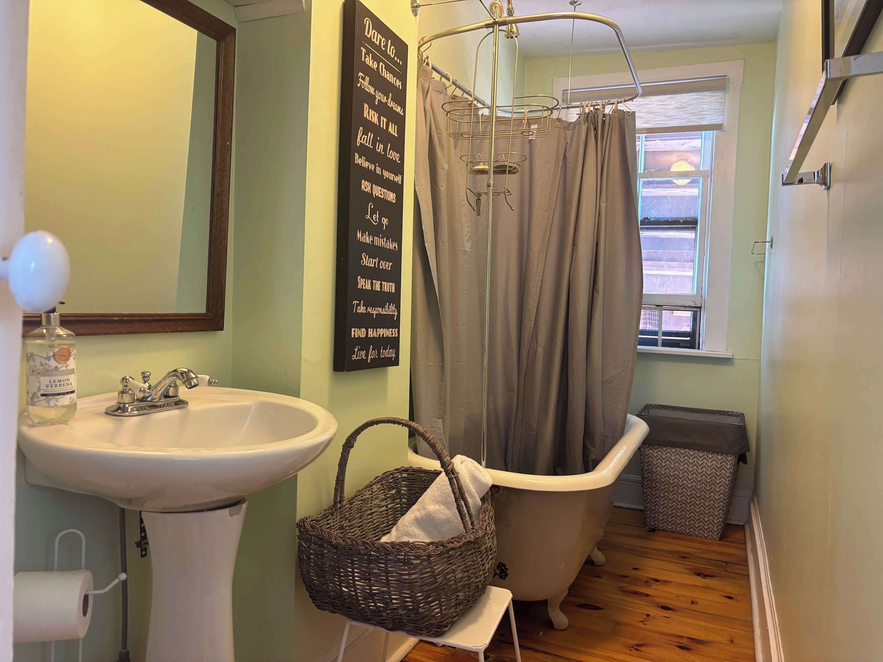 A bathroom with a white sink, a wicker basket, a shower curtain, and a motivational quote on the wall.