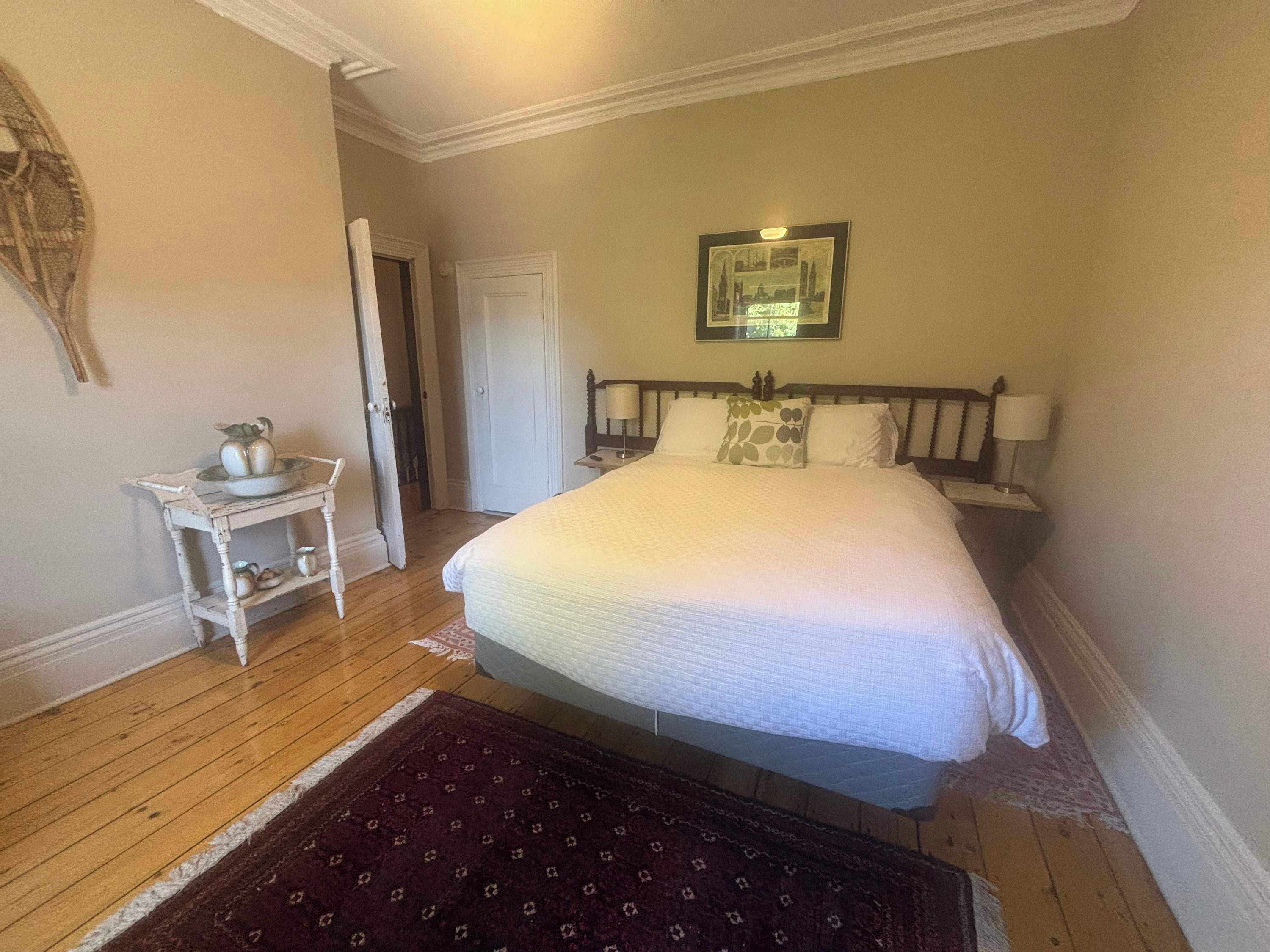 Une chambre à coucher avec un lit, des tables de chevet, une commode, un tapis et un tableau encadré au mur.