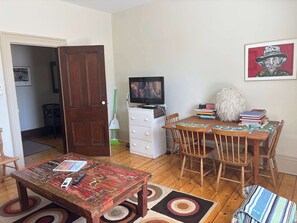 A living room with a wooden table, chairs, a television, a bookshelf, and a door. - Pentz Howe House Apartment, (Charlottetown)