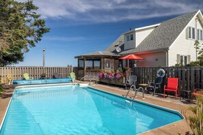 A swimming pool with a covered patio area, a wooden fence, and outdoor seating. - Waterfront renovated Cottage with heated Pool (Mount Stewart)