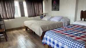 Quarto com duas camas, piso de madeira, uma cadeira e uma janela com cortinas.