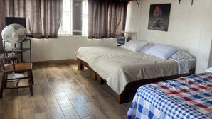 Quarto com cama, cadeira, ventoinha, prateleira e janela com cortinas.