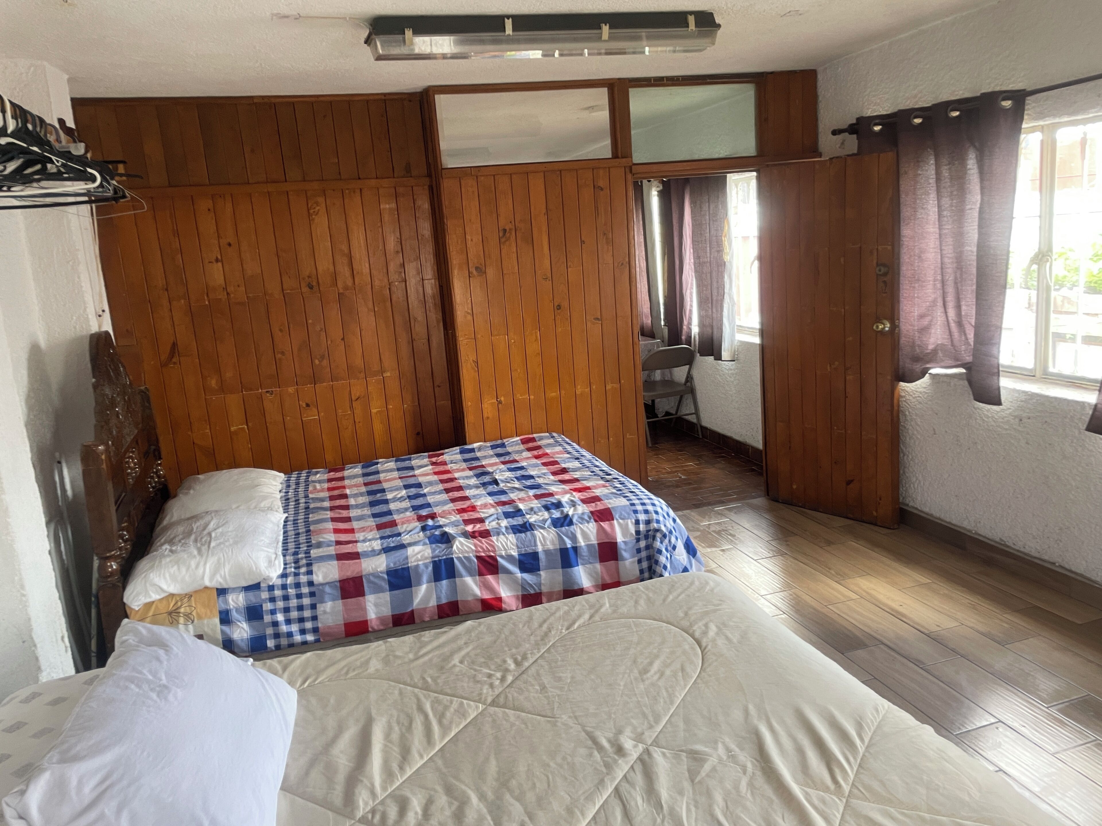 Une pièce avec un lit, des murs lambrés, une fenêtre avec des rideaux et une chaise.