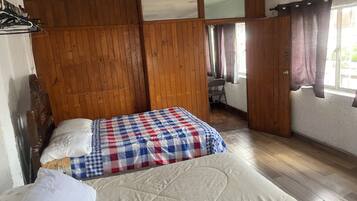 Une pièce avec un lit, des murs lambrés, une fenêtre avec des rideaux et une chaise.
