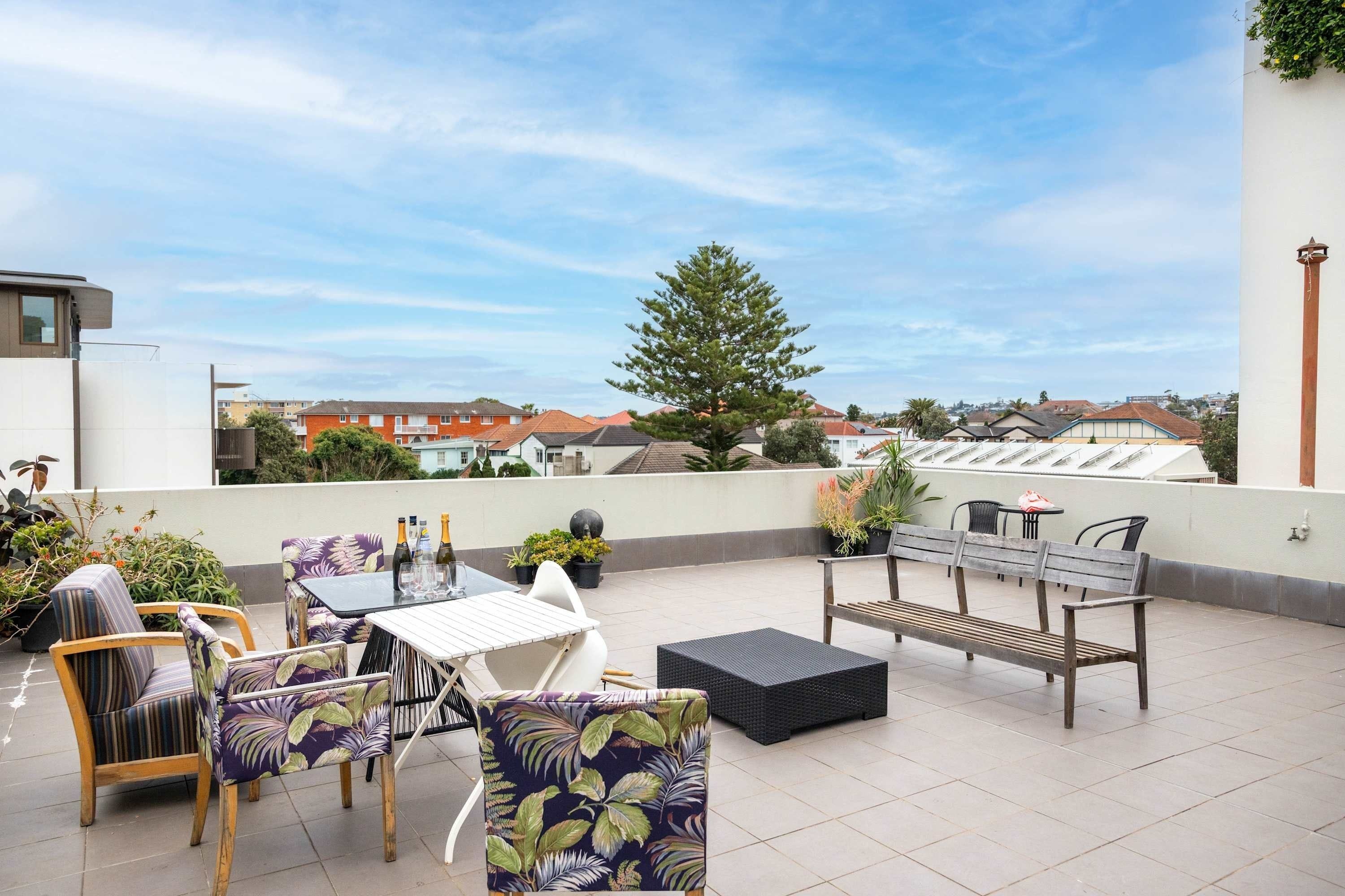Eine Dachterrasse mit Gartenmöbeln, Blumentöpfen und Blick auf die Nachbarschaft.