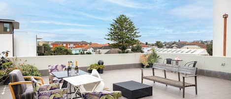 A rooftop terrace with outdoor furniture, potted plants, and a view of the neighborhood.