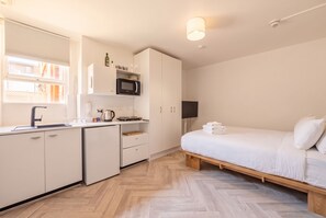 A compact hotel room with a kitchenette, a bed with white linens, and a wooden floor. - Bondi Studio, Rooftop Terrace | 2 Min Walk to Beach, King Bed, AC (Bondi Beach)
