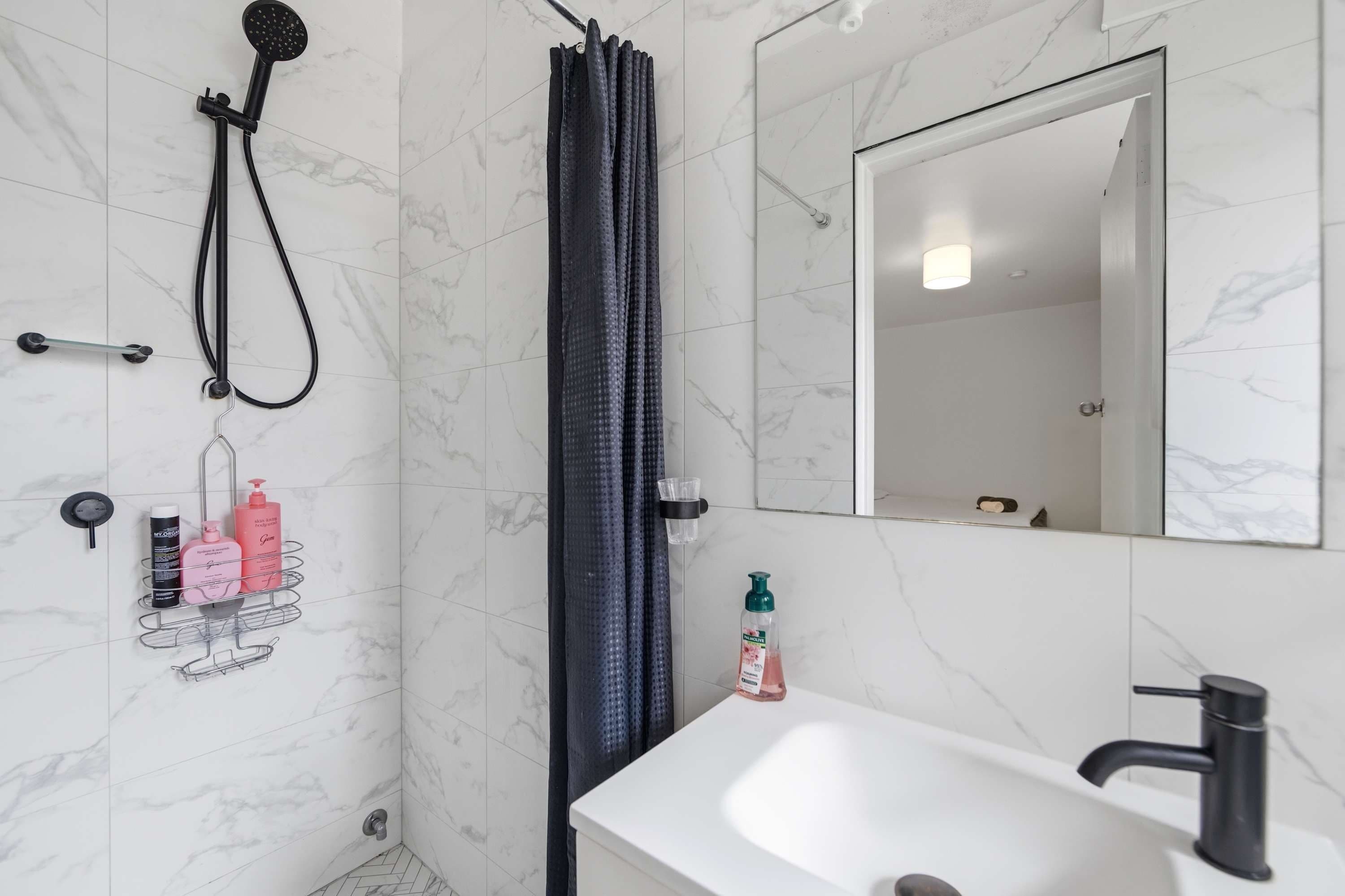 A bathroom with a shower, a sink, a mirror, and toiletries on a rack.