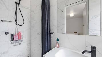 A bathroom with a shower, a sink, a mirror, and toiletries on a rack.