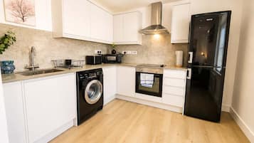 Een moderne keuken met witte kastjes, een roestvrijstalen wasmachine, een magnetron, een oven en een zwarte koelkast.