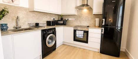 A modern kitchen with white cabinets, a stainless steel washing machine, a microwave, an oven, and a black refrigerator.