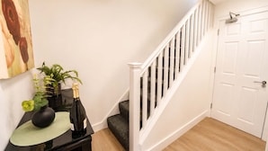 A staircase with white railings leading to a door, a black console table with a vase and a bottle, and a painting on the wall. - Spacious 3BR Flat Sleeps 10 for Groups & Family (Cardiff)