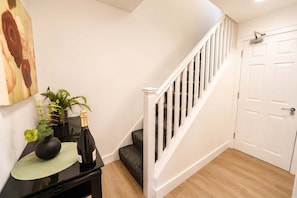 Eine Treppe mit weißen Geländern führt zu einer Tür, ein schwarzer Konsolentisch mit einer Vase und einer Flasche sowie ein Gemälde an der Wand.