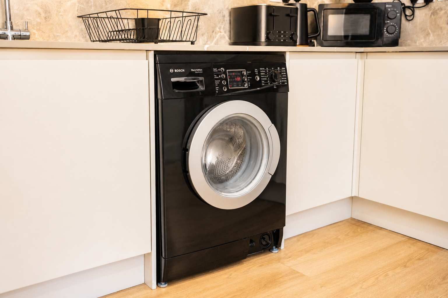 Un lave-linge compact et moderne, installé dans une cuisine, avec un four à micro-ondes placé au-dessus.