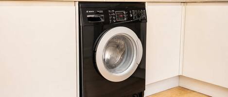 Un lave-linge compact et moderne, installé dans une cuisine, avec un four à micro-ondes placé au-dessus.