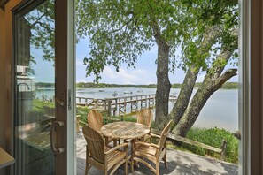 A wooden deck with a table and chairs overlooking a lake with boats. - Waterfront Cape Cottage w/ Private Beach Access (Dennis)
