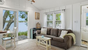 En hyggelig stue med en sofa, et lille bord og udsigt til en sø gennem store vinduer.