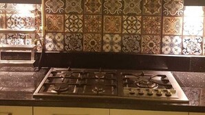 A kitchen with a gas stove, yellow cabinets, and patterned tile backsplash. - Spacious 3-bedroom apartment in charming Cairo with AC (Cairo Governorate)