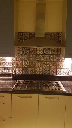 A kitchen with a gas stove, yellow cabinets, and patterned tile backsplash. - Spacious 3-bedroom apartment in charming Cairo with AC (Cairo Governorate)