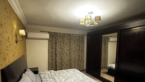 A bedroom with a bed, a wardrobe, a mirror, and a chandelier. - Spacious 3-bedroom apartment in charming Cairo with AC (Cairo Governorate)