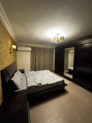 A bedroom with a bed, a wardrobe, a mirror, and a chandelier. - Spacious 3-bedroom apartment in charming Cairo with AC (Cairo Governorate)