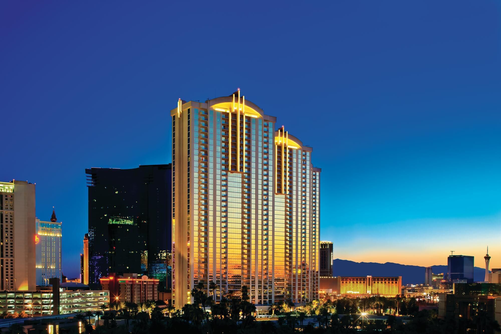 A high-rise hotel with multiple floors, a prominent entrance, and a view of the surrounding cityscape at dusk.
