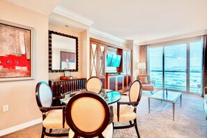 A hotel room with a dining area, a TV, a large window with a view, and a decorative wall piece. - Luxury MGM Signature 1BR/2BA Suite - Strip & Mountain View - NO Resort Fee (Las Vegas)