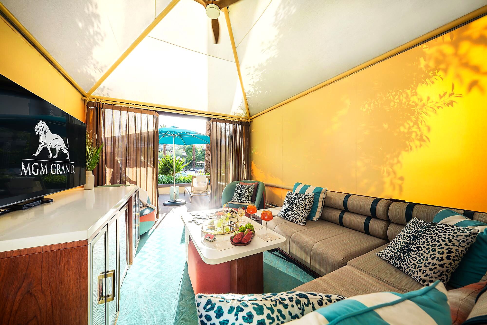 A room with a television displaying the MGM Grand logo, a sofa with leopard print cushions, and a dining area with a table set for two.