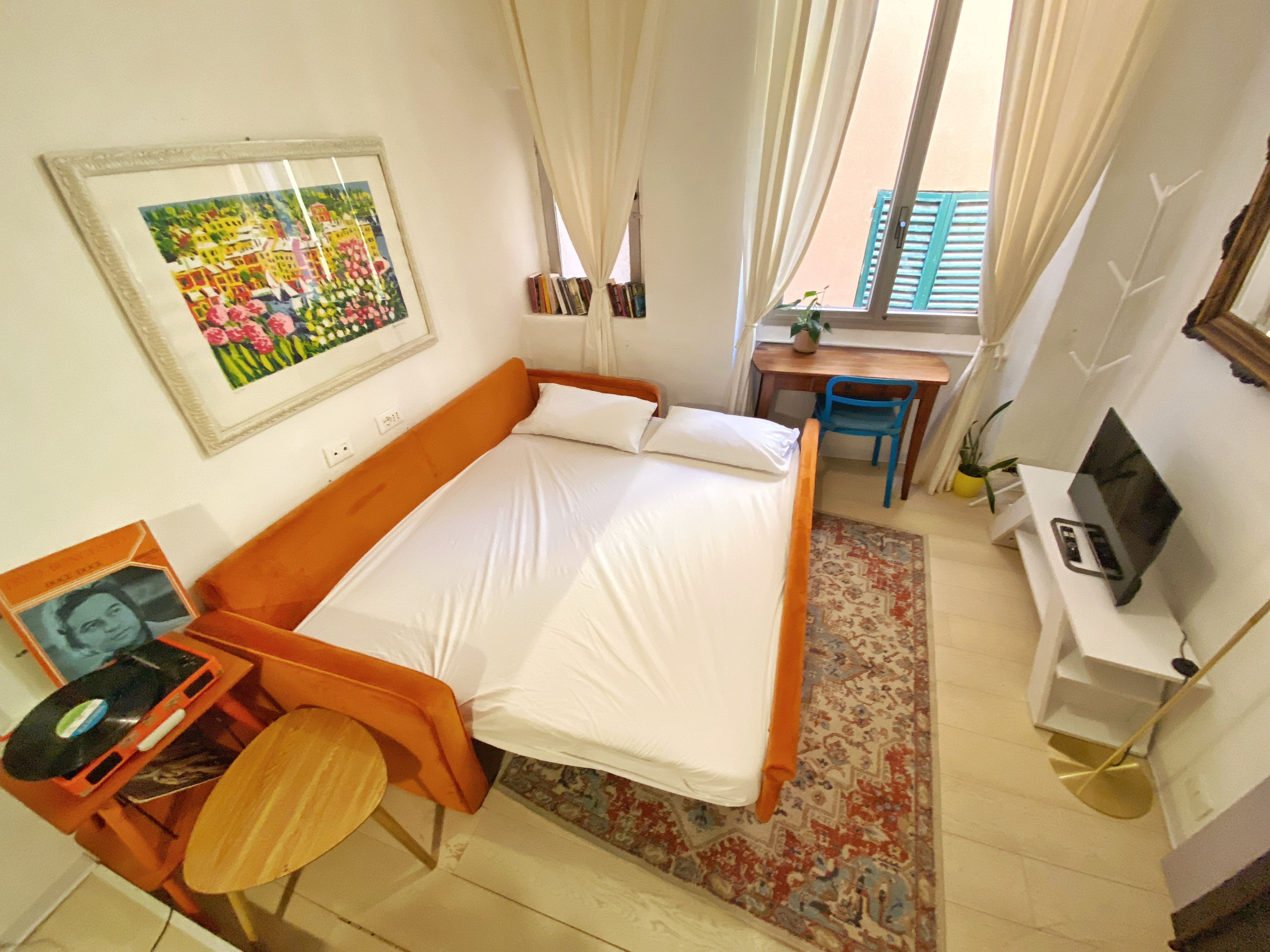 A bedroom with a bed, a desk, a chair, a television, and a framed picture on the wall.