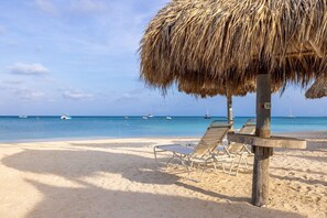 A beach with thatched umbrellas, lounge chairs, and a clear view of the sea with boats. - Aruba Marriott Surf Club - Oceanside 1 bedroom Studio with kitchenette, sleeps 4 (Noord)