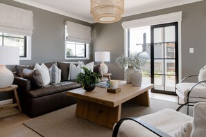 A living room with a brown leather sofa, a wooden coffee table, and a white armchair. - The Farmhouse; Hauraki Views & Tranquil Luxury (Matakana)