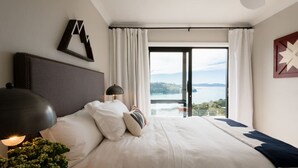 Habitación de hotel con una cama grande, una mesita de noche con lámpara, vista a un cuerpo de agua a través de una puerta de vidrio y un adorno en la pared.