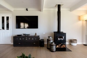 A living room with a black fireplace, a television mounted on the wall, and a dark wooden dresser. - The Farmhouse; Hauraki Views & Tranquil Luxury (Matakana)