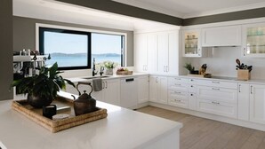 Una cocina moderna con armarios blancos, un ventanal con vista a un cuerpo de agua y una cafetera.