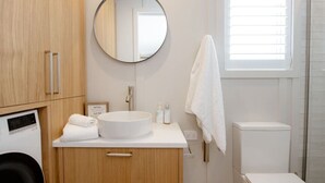 Ein Badezimmer mit einem hölzernen Waschtisch, einem runden Spiegel, einem weißen Waschbecken und einem Handtuch an der Wand.