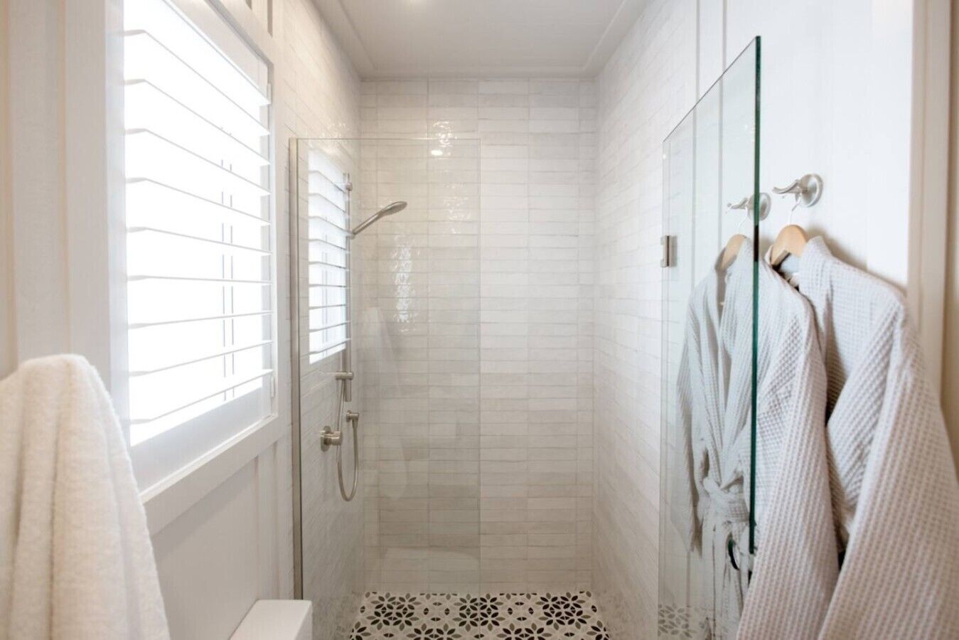 Un baño moderno con ducha envuelta en vidrio, paredes cubiertas de azulejos blancos y un inodoro a la vista.