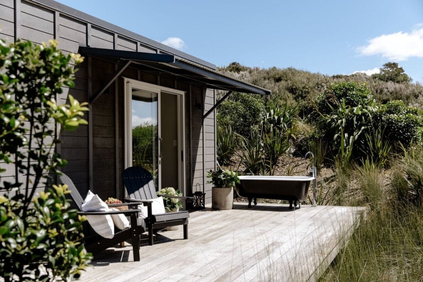 A deck with a chair and a bathtub, surrounded by greenery.