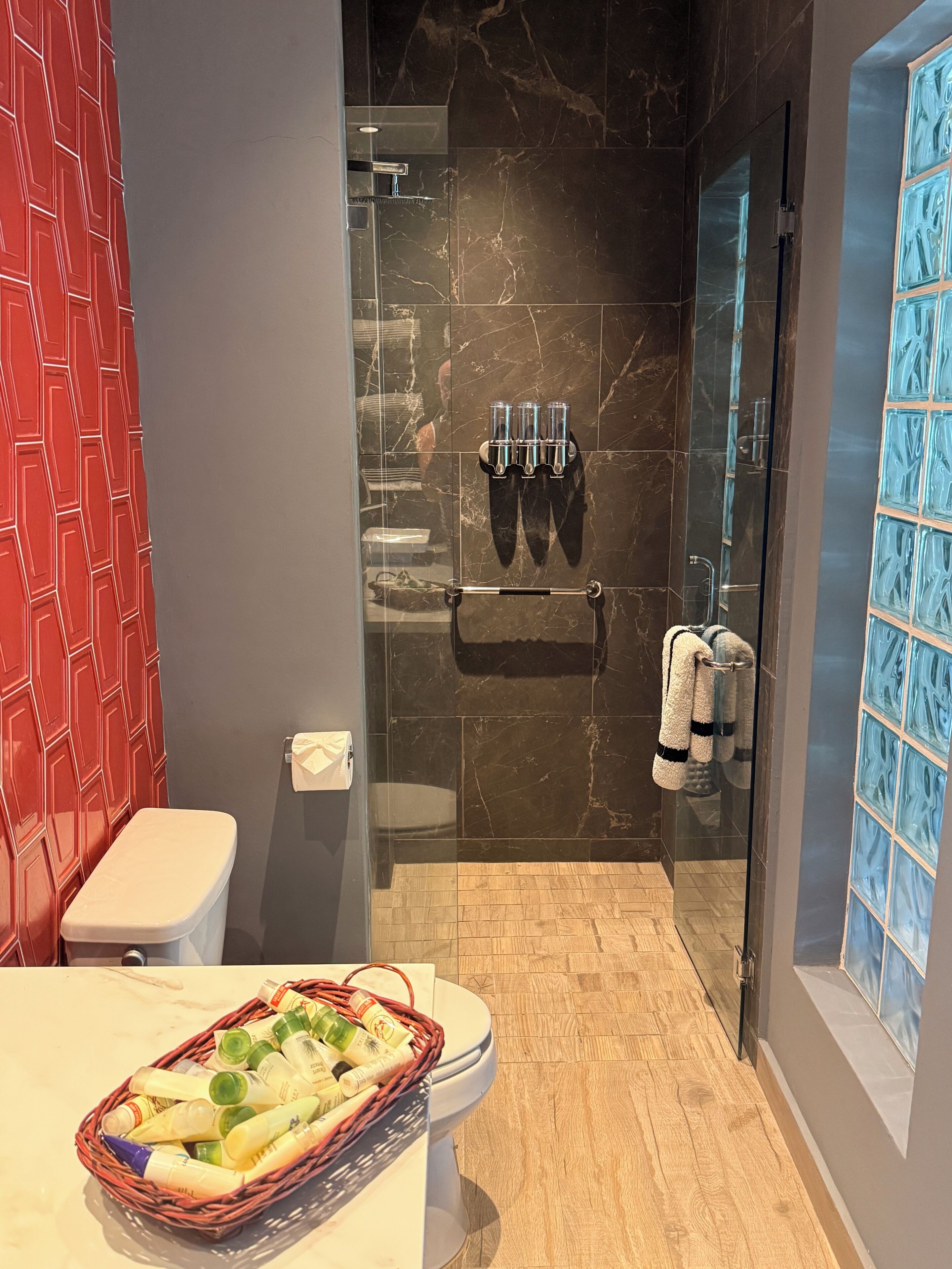A modern bathroom with a glass-enclosed shower, a toilet, and a wicker basket of toiletries.