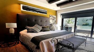 A modern bedroom with a large bed, a bench, a nightstand, and a view of the outdoors through a glass door.