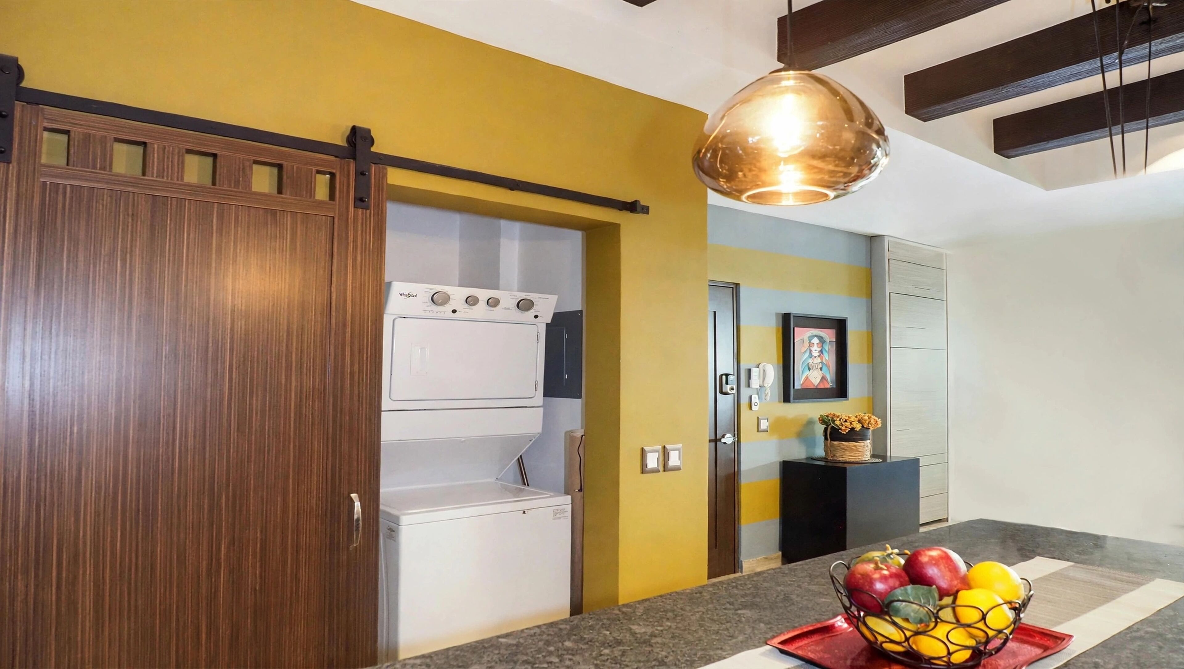 A kitchen with a washing machine, a fruit bowl on the counter, and a sliding door.